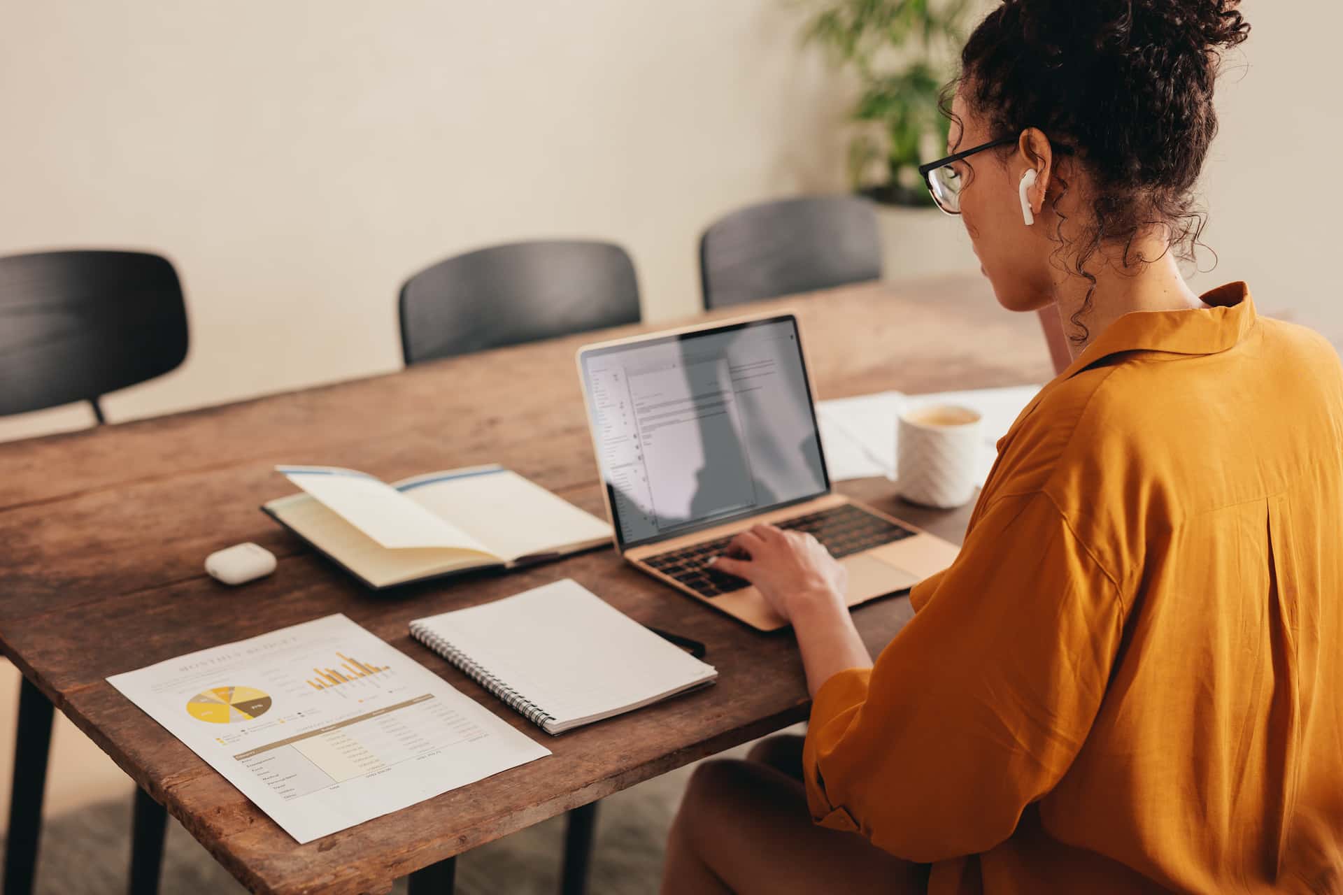 Woman working from home at dining table with sheets of paper and laptop outlining expenses to monitor tax deduction claims